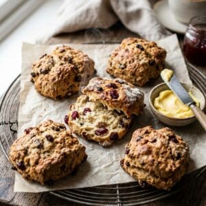 Frisch gebackene, goldbraune Sauerteig-Scones mit getrockneten Cranberries und Sultaninen auf einem Kuchengitter, serviert mit Butter.